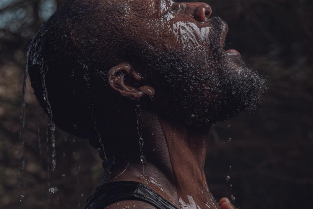 A close-up profile of a person with water running over their face and head against a dark background.